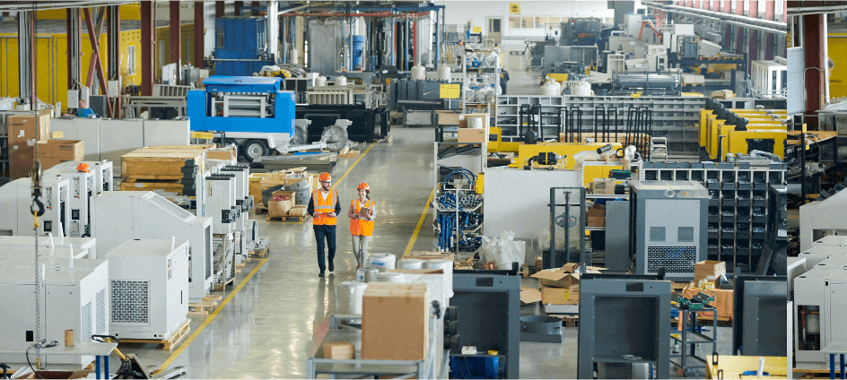 Two workers wear orange safety jackets and walk down a warehouse hallway